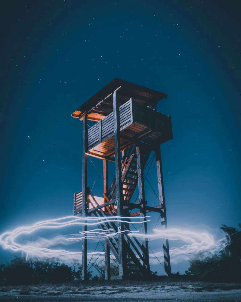 Light trails around a wooden lookout tower under a starry sky